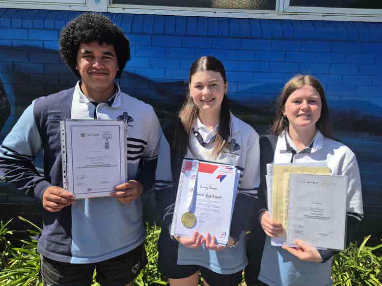 Three Year 12 students who received special awards standing in front of school mural