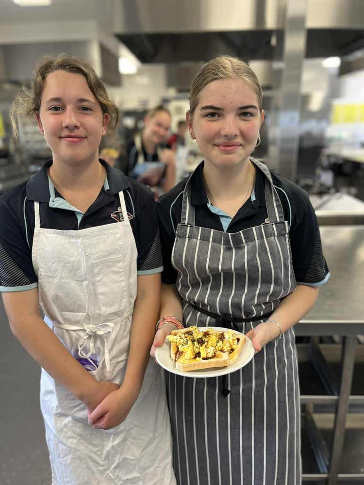 Two girls are proudly showing off their scrambled eggs cooked in the school Hospitality Rooms